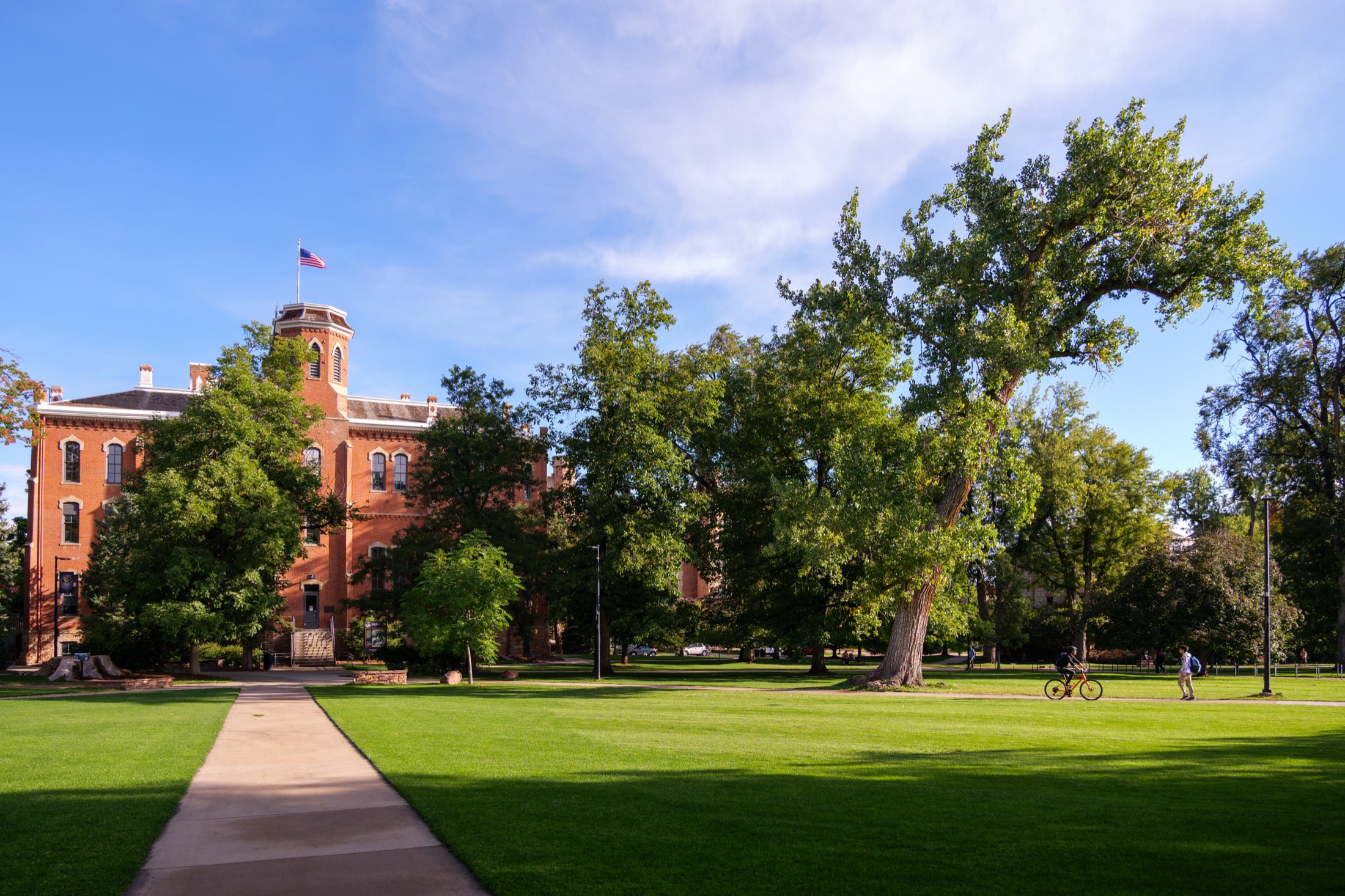 A wide CU Boulder lawn with a red-brick academic building and students crossing the quad.